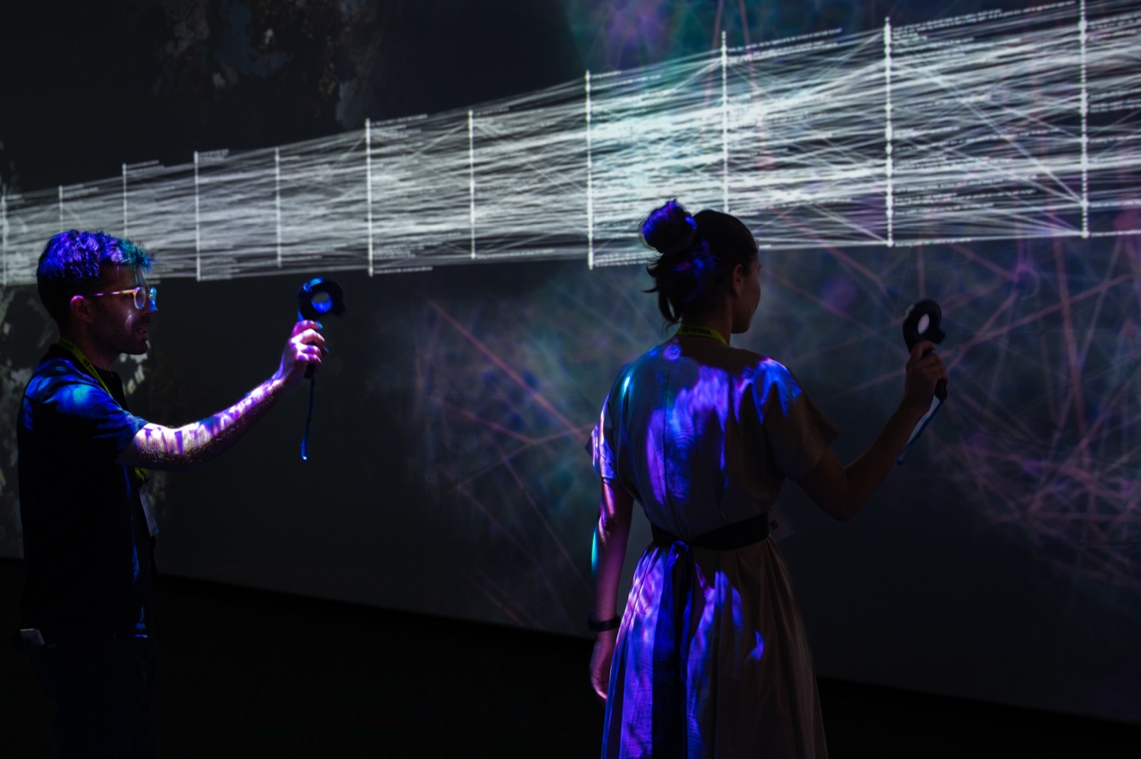 Two visitors holding handheld controllers, drawing bright filaments across a projected citation network