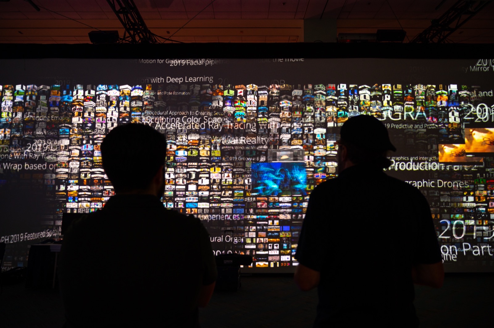 Thousands of paper teaser thumbnails tiled across the wall, with 2019 titles such as Sculpting Color Spaces and RTX Accelerated Ray Tracing floating over them